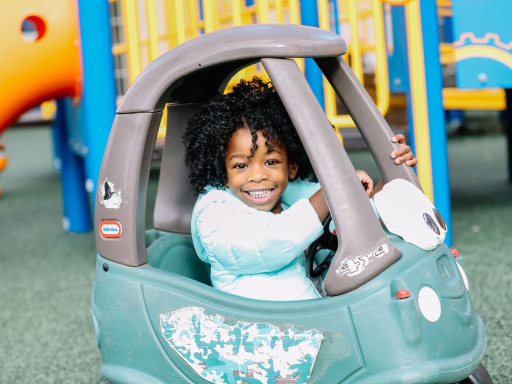 Little girl with special needs rides in little car on playground