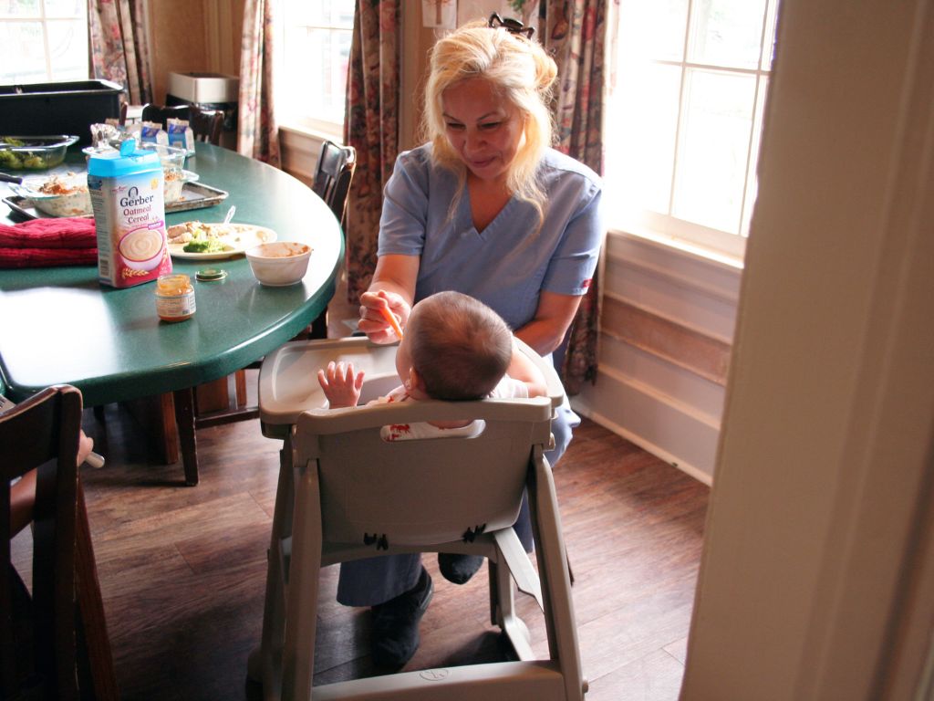 Nurse caregiver feeds infant with special needs in high chair