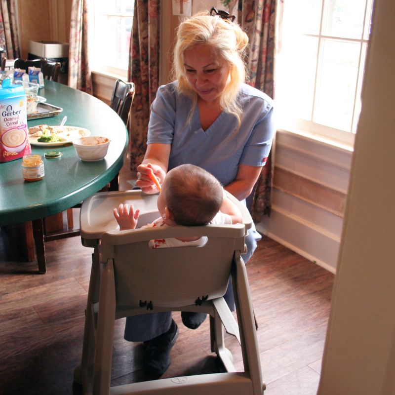 Woman caregiver feeds a baby with special needs.